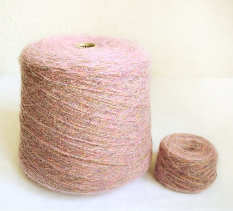 May include: Two spools of yarn. The larger spool is a light pink color with a cylindrical shape. The smaller spool is also light pink and round. Both spools have a soft, fuzzy texture and are suitable for knitting or crocheting projects.