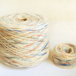 Puede incluir: Dos ovillos de hilo, uno grande y otro pequeño, de color crema con motas azules, melocotón y marrones.