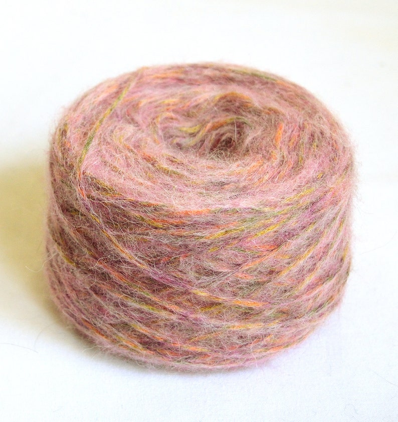 May include: A ball of yarn in shades of pink, orange, and green. The yarn appears soft and fluffy, ideal for knitting or crocheting projects. The colors are blended, creating a textured appearance.