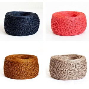 May include: Four individual balls of yarn arranged in a grid. The top left ball is dark navy blue, the top right is a vibrant coral red, the bottom left is a warm golden brown, and the bottom right is a neutral light beige or tan colour.