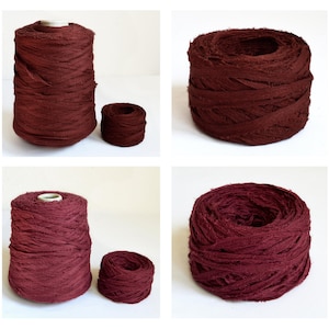 Op de afbeelding: Twee spoelen met bordeauxrode stofdraad, een grote en een kleine. De draad is gemaakt van dunne stroken stof die met elkaar zijn gedraaid.