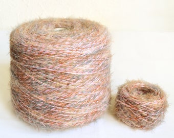 Puede incluir: Dos ovillos de hilo, uno grande y otro pequeño, en una mezcla multicolor de marrón, rosa y gris. El hilo tiene una textura peluda.