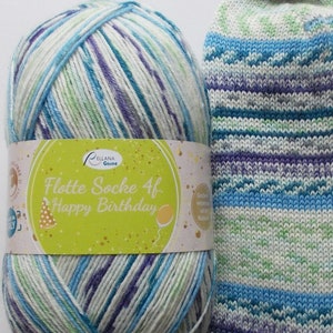 Könnte beinhalten: Eine weiße Garnrolle mit blauen, grünen und violetten Streifen. Das Garn ist mit "Flotte Socke 4f. Happy Birthday" beschriftet.