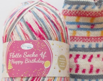 May include: A ball of colorful yarn with a label that reads "Flotte Socke 4f. Happy Birthday". The yarn is a mix of white, pink, blue, and gray. A knitted sock with a colorful pattern is shown next to the yarn.