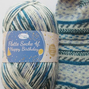 Könnte beinhalten: Ein Knäuel Wolle mit dem Etikett "Flotte Socke 4f. Happy Birthday" neben einer gestrickten Socke. Das Garn ist eine Mischung aus Weiß, Blau und Türkis. Die Socke hat ein ähnliches Farbschema mit einem geometrischen Muster.