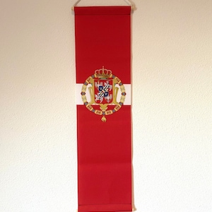 Könnte beinhalten: Ein rotes Banner mit einem weißen und goldenen Wappen, das eine Krone, einen Schild mit einem Kreuz und zwei Löwen zeigt. Das Banner hängt an einer weißen Schnur.