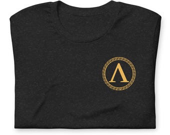 Puede incluir: Camiseta negra con una letra griega 'A' dorada dentro de un círculo con un borde de llave griega.