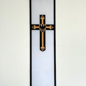 以下が含まれることがあります： 黒い縁取りと中央に黒い鷲の付いた金の十字架が描かれた白いバナー。バナーは木製の棒に吊るされています。