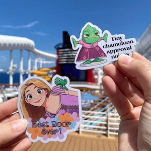 May include: Two die-cut vinyl stickers. One features a green chameleon in a pink dress with the text Tiny chameleon approval noises. The other shows a blonde character with a small green chameleon on their shoulder, wearing a purple dress with the text Best Door Ever! surrounded by orange and purple flowers.