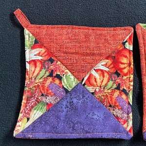 May include: A pair of orange and purple quilted pot holders with a fall-themed fabric design. The fabric features pumpkins, gourds, and leaves.