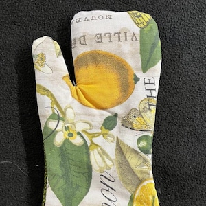 May include: A green and white oven mitt with a lemon and butterfly design. The text "VILLE DE" and "NOVOA" are printed on the mitt.