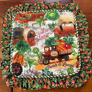 Puede incluir: Un salvamanteles de tela verde, rojo y negro con un camión vintage, animales de granja y verduras. El texto "Field to Feast" y "Fresh & Local" está impreso en el salvamanteles.