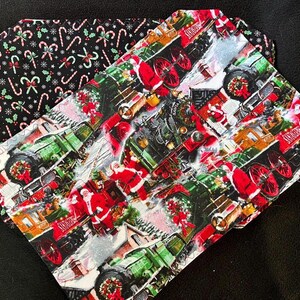 Puede incluir: Una tela navideña con un patrón repetido de locomotoras de vapor de estilo vintage que tiran de vagones de tren decorados con acebo y bastones de caramelo. Santa Claus está representado en la escena, junto con la nieve y un patrón de bastones de caramelo en blanco y negro en el fondo.