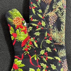May include: A pair of black oven mitts with a Christmas-themed design. The mitts feature holly leaves, red berries, pine branches, and pine cones.