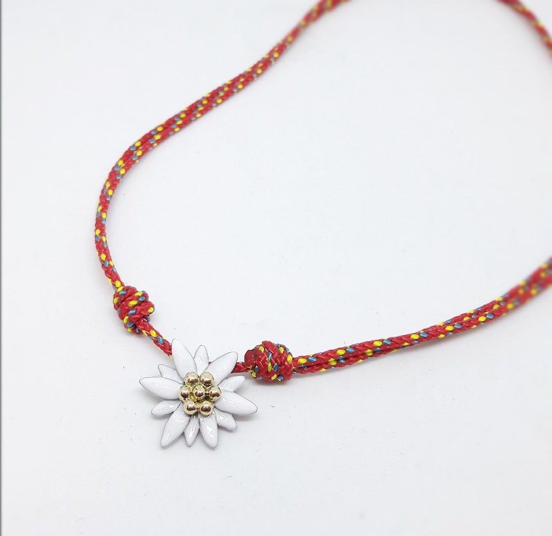 May include: A red and yellow rope bracelet with a white edelweiss flower charm.