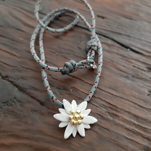 May include: A gray and orange rope necklace with a white edelweiss flower pendant. The flower has a gold center with small gold beads.
