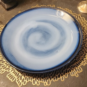 May include: A blue and white ceramic dinner plate with a swirl design sits on a gold metal charger.