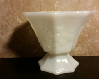 May include: White milk glass pedestal bowl with a floral design. The bowl is octagonal in shape and has a scalloped edge.