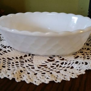 May include: White milk glass bowl with a wavy rim and a textured design. The bowl is sitting on a white crocheted doily.