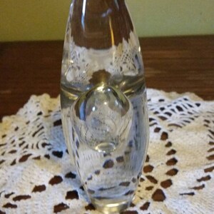 May include: A clear glass pipe with a round bowl and a long, narrow stem. The pipe is sitting on a white crocheted doily.