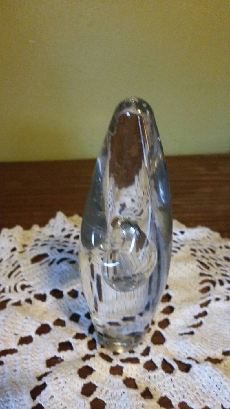 May include: A clear glass sculpture with a rounded, organic shape. The sculpture has a smooth, polished surface and appears to be hand-blown.