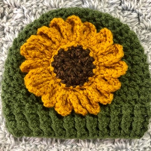May include: A green crocheted hat with a yellow crocheted sunflower on top.