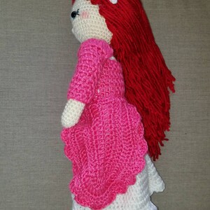 May include: A crocheted doll with long red hair, a pink dress, and a white flower in her hair.