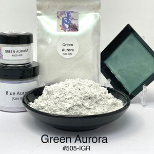 May include: A white powder pigment called Green Aurora, labeled #505-IGR, is shown in a black bowl. A smaller jar of the same pigment is shown in the background, along with a larger bag of the pigment and a small square dish.