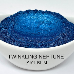 May include: A close-up of a white ceramic bowl filled with a shimmering, deep blue powder. The powder is labeled "Twinkling Neptune" with the code #101-BL-M. The powder has a metallic, glittery appearance.