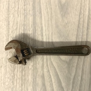 May include: A vintage metal adjustable wrench with a weathered finish. The tool features a knurled adjustment screw and is embossed with the text BARCALO-BUFFALO and MADE IN U.S.A. on the handle, which includes a circular hole at the end.