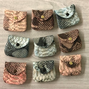 May include: Ten small, zippered pouches made of snakeskin patterned fabric in various colors, including brown, pink, blue, and gray. Each pouch has a gold zipper pull and a gold button closure.