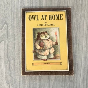 K&ouml;nnte beinhalten: Ein Kinderbuch mit dem Titel "Owl at Home" von Arnold Lobel. Das Cover zeigt eine Illustration einer Eule mit einer Kerze und einem Buch, vor einem gelben Hintergrund mit braunen R&auml;ndern. Das Buch weist Gebrauchsspuren auf.