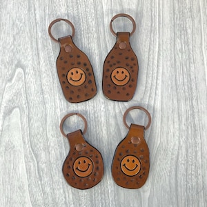 May include: Four brown leather keychains with a smiley face design. Each keychain has a copper-colored ring.