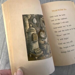 K&ouml;nnte beinhalten: Ein offenes Buch mit Illustrationen und Text. Die linke Seite zeigt eine detaillierte Schwarz-Wei&szlig;-Illustration einer eulenartigen Figur in der N&auml;he eines Ofens. Die rechte Seite tr&auml;gt den Titel "TEAR-WATER TEA" und Text &uuml;ber die Eule.