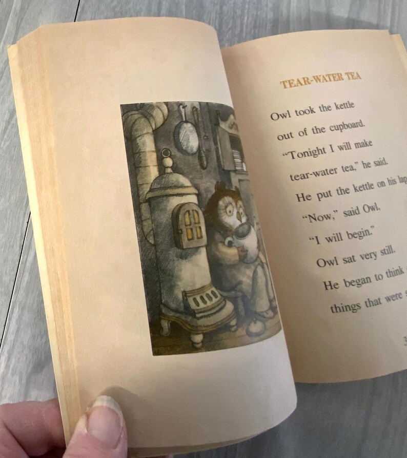 K&ouml;nnte beinhalten: Ein offenes Buch mit Illustrationen und Text. Die linke Seite zeigt eine detaillierte Schwarz-Wei&szlig;-Illustration einer eulenartigen Figur in der N&auml;he eines Ofens. Die rechte Seite tr&auml;gt den Titel "TEAR-WATER TEA" und Text &uuml;ber die Eule.