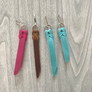 May include: Four leather keychains with braided designs in pink, brown, blue, and turquoise. Each keychain has a silver metal loop.