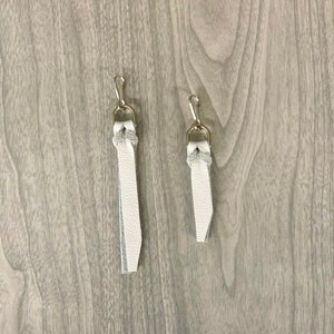 May include: Two white leather keychains with silver metal clasps. The keychains are different lengths.