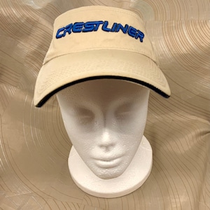 May include: A beige visor with a black trim and blue embroidered text that reads "CRESTLINER".