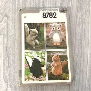 May include: Simplicity pattern 8782 featuring four stuffed animal designs: a squirrel, an owl, a skunk, and a chipmunk. The pattern is for one size. The cover is gray with the pattern number in large black text.