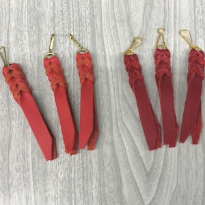 May include: Six red leather keychains with gold metal clasps. The keychains are braided and have a tassel-like fringe at the end.