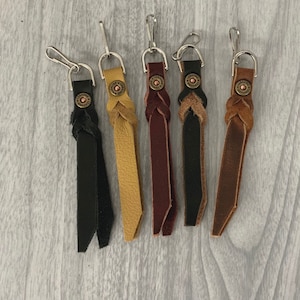 May include: Five leather keychains with a braided design and a metal loop. Each keychain has a different color: black, brown, red, yellow, and tan.