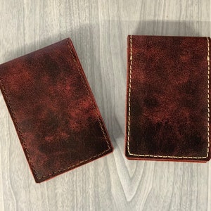 May include: Two brown leather wallets with white stitching. The wallets are closed and have a distressed look.