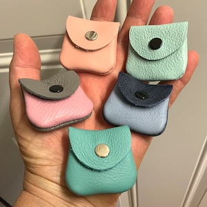 May include: Six small leather pouches in various colors, including pink, blue, and green. Each pouch has a flap with a snap closure and a small metal button.