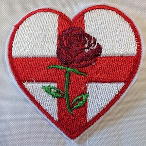 May include: Embroidered heart-shaped patch. It features a red cross on a white background, with a burgundy rose at the centre. The rose has green leaves and stem. The patch has a white border.