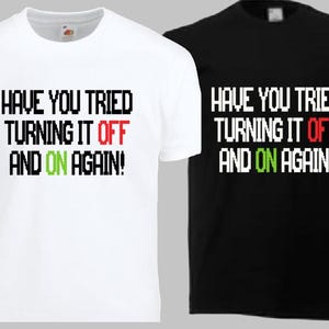 May include: A white t-shirt and a black t-shirt, each featuring the pixelated text "HAVE YOU TRIED TURNING IT OFF AND ON AGAIN!" with the word "OFF" in red and the word "ON" in green, printed in a blocky, computer-style font on the chest.