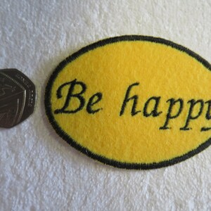 May include: Yellow felt oval patch with black stitching around the edges. The patch has black embroidery that reads "Be happy".