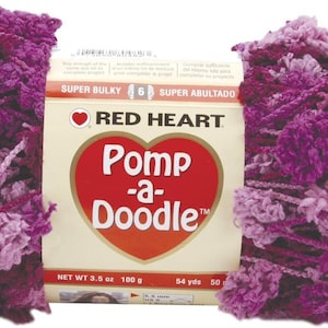 May include: A skein of Red Heart Pomp-a-Doodle yarn in shades of purple and pink. The yarn is super bulky and has a textured, pom-pom-like appearance. The packaging features the brand name and product details.
