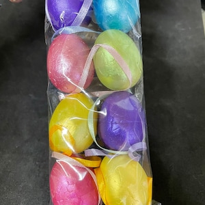 May include: A package of six iridescent Easter eggs in various colors, including purple, blue, pink, yellow, and green. The eggs are tied together with ribbons.