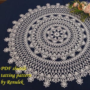 May include: A detailed, white, circular doily with a floral design, resting on a dark blue surface. The doily is made with a delicate, lace-like pattern. The text "PDF shuttle tatting pattern by Renulek" is in the lower left corner.
