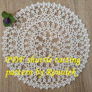 May include: White crochet doily with a delicate floral pattern. The doily is round and has a diameter of approximately 12 inches. The text "PDF shuttle tatting pattern by Remulek" is visible in the lower part of the image.
